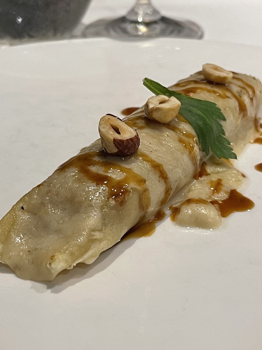 Canelón enrollado con avellanas y perejil sobre plato blanco