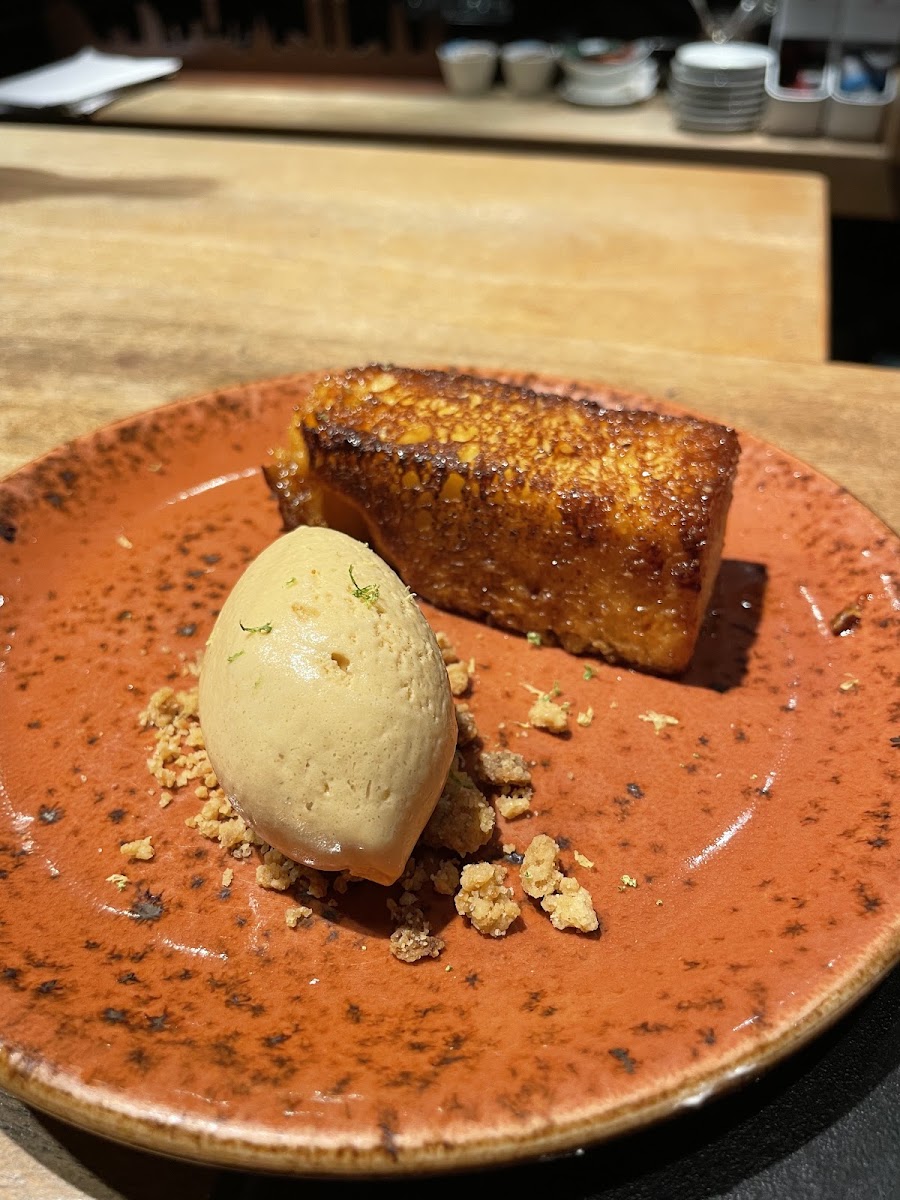 Brioche dorado con bola de helado y crumble sobre plato naranja