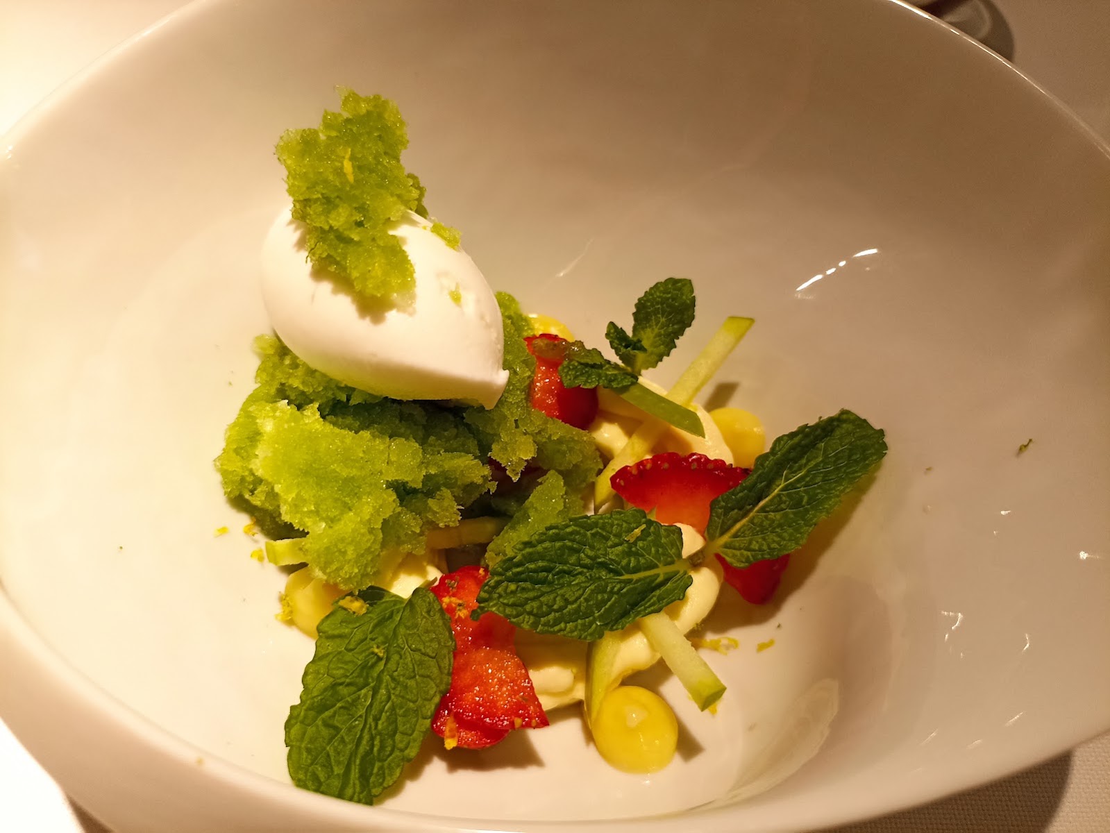 Cuenco blanco con fruta laminada, menta, granizado verde y crema