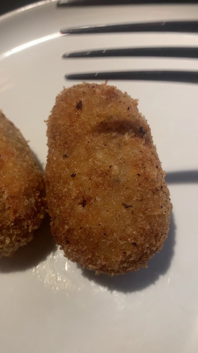 Dos croquetas empanadas sobre plato blanco con trazos de salsa oscura