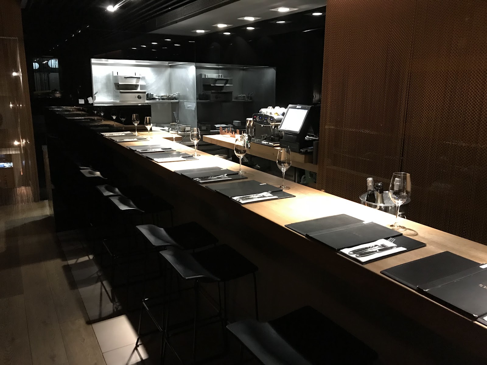La barra de roble de Coure frente a la cocina abierta, con la pared de malla de cobre